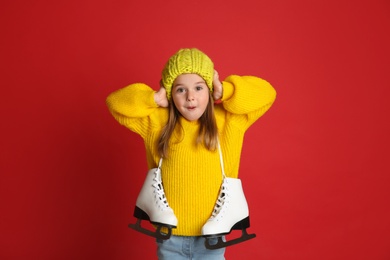 Photo of Excited little girl in yellow knitted sweater with skates on red background