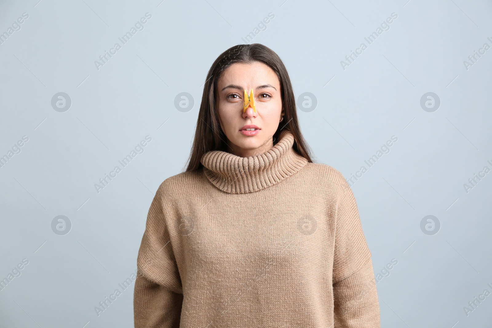 Photo of Young woman with clothespin on light grey background. Runny nose concept