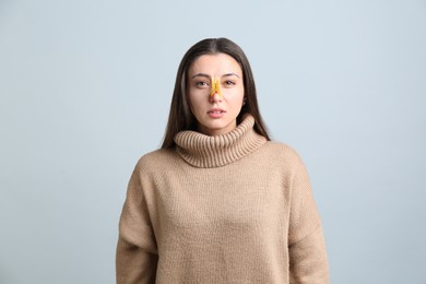 Young woman with clothespin on light grey background. Runny nose concept