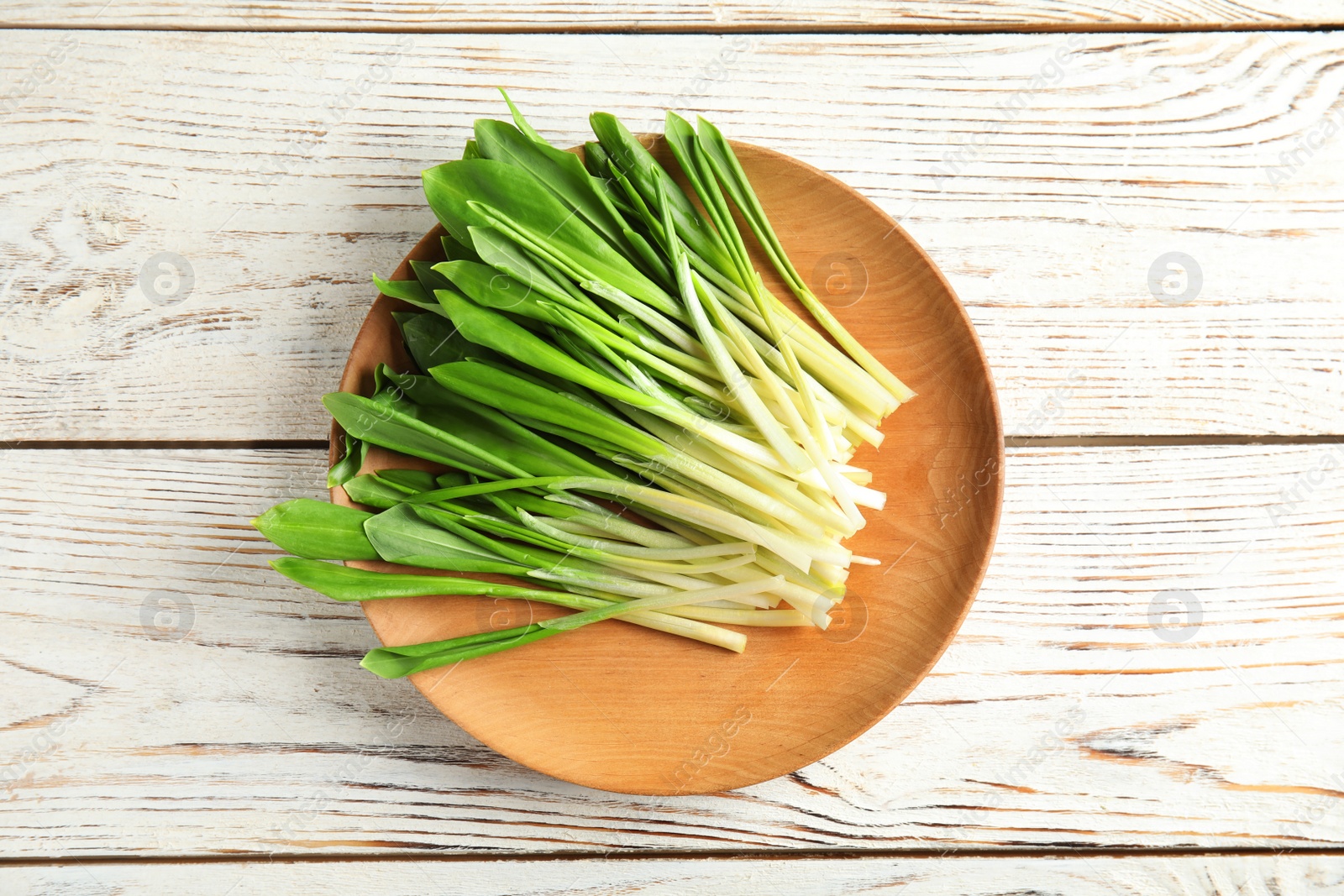 Photo of Plate with wild garlic or ramson on wooden table, top view