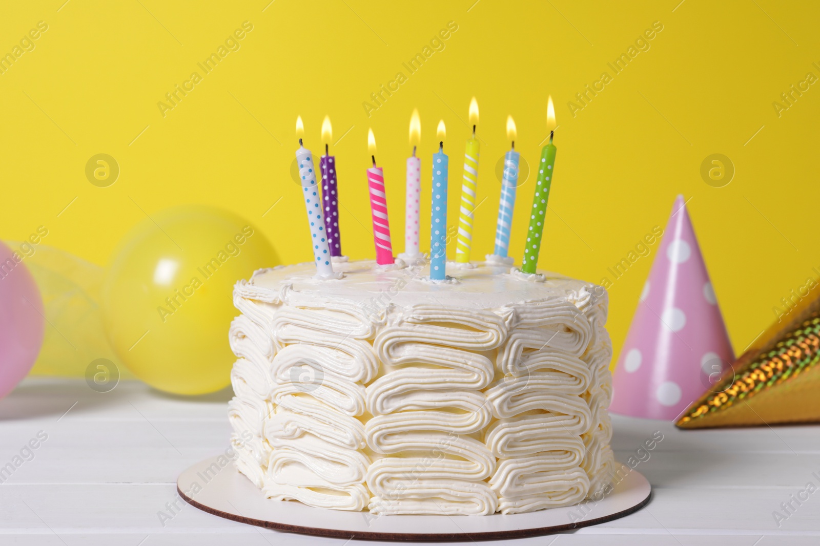 Photo of Delicious cake with burning candles and festive decor on white wooden table