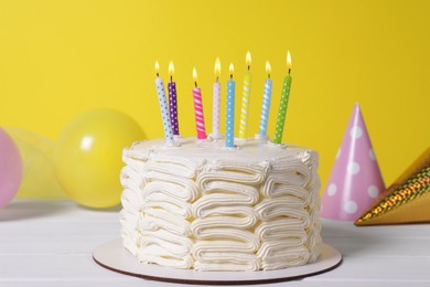 Delicious cake with burning candles and festive decor on white wooden table