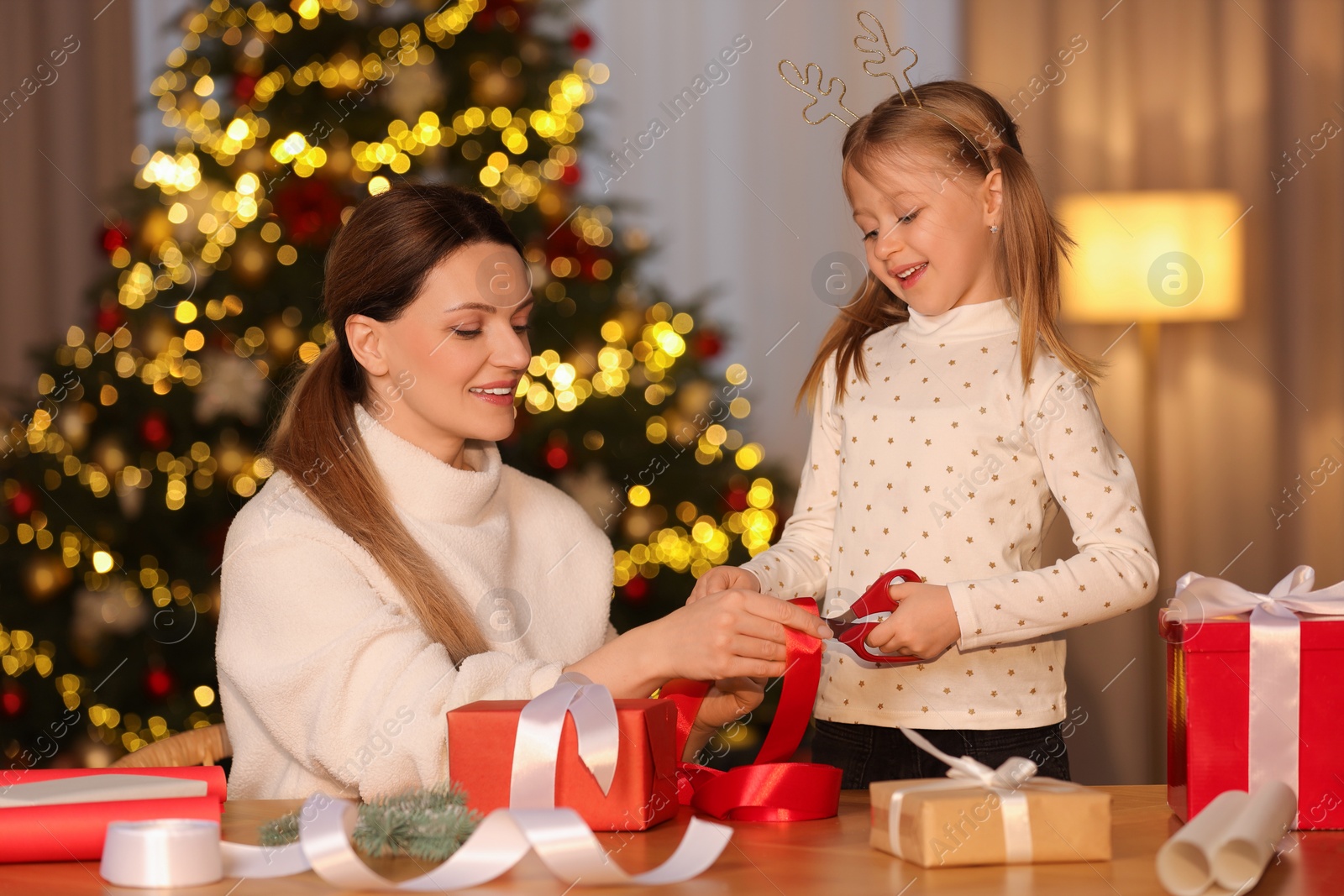 Photo of Christmas presents wrapping. Mother and her little daughter decorating gift box with ribbon at home