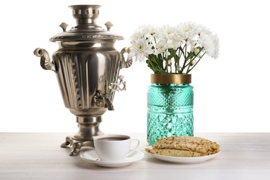 Photo of Vintage samovar, cuphot drink, pancakes and vase with flowers on wooden table against white background. Traditional Russian tea ceremony