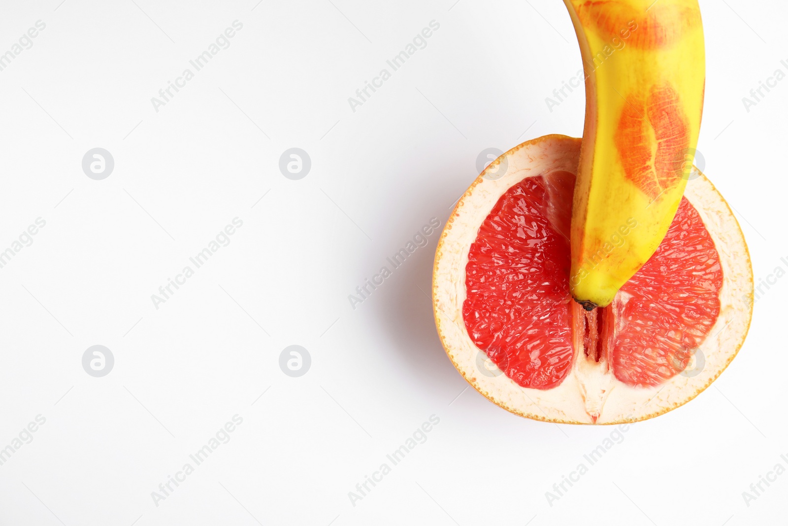 Photo of Fresh grapefruit and banana with red lipstick marks on white background, top view. Sex concept