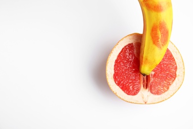 Fresh grapefruit and banana with red lipstick marks on white background, top view. Sex concept