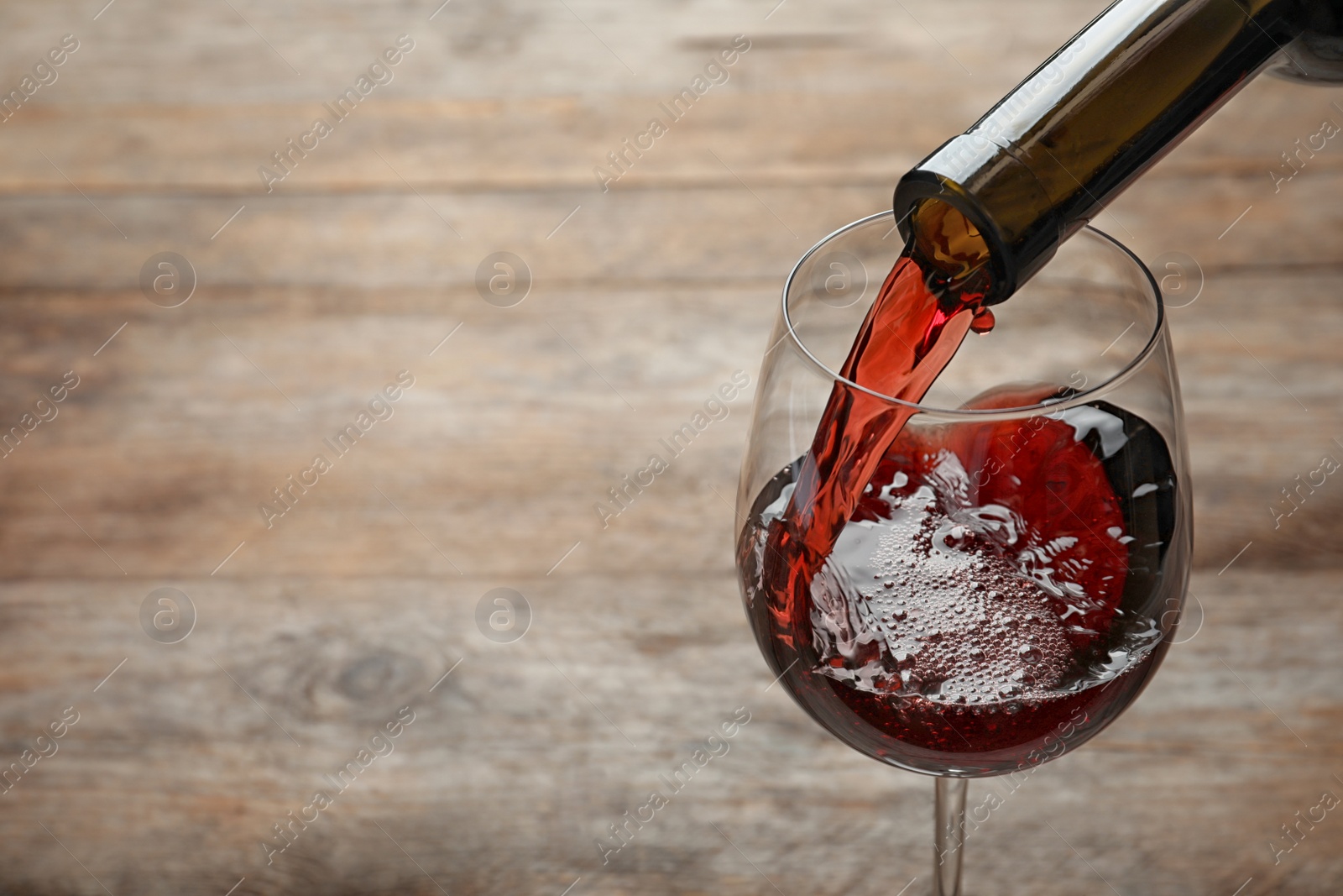 Photo of Pouring red wine from bottle into glass on wooden background. Space for text