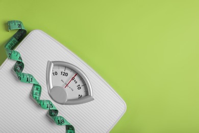 Photo of Weight loss concept. Scales and measuring tape on green background, top view. Space for text