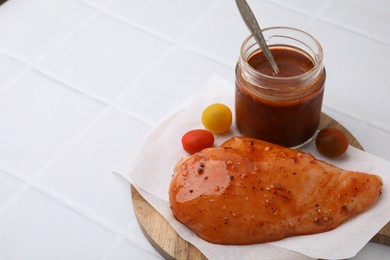 Photo of Fresh marinade and raw chicken fillets on white tiled table. Space for text