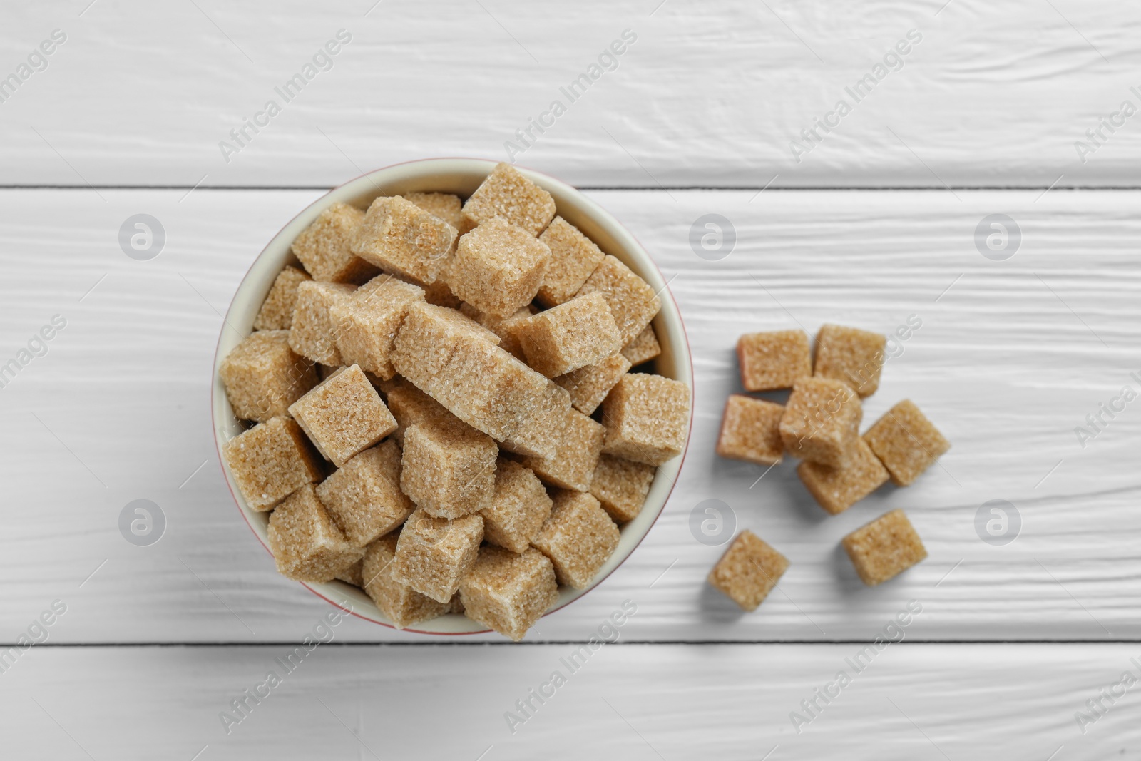 Photo of Brown sugar cubes in bowl on white wooden table, top view