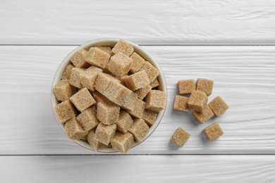 Photo of Brown sugar cubes in bowl on white wooden table, top view