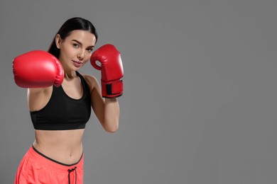 Photo of Beautiful woman in boxing gloves training on grey background. Space for text