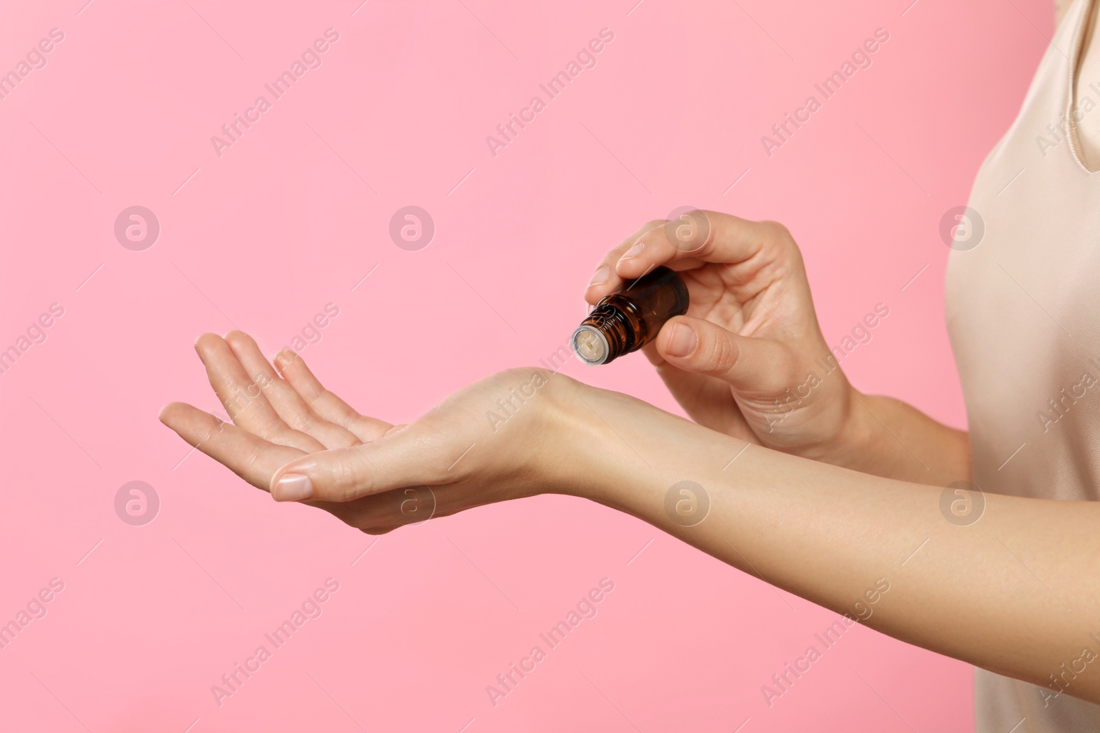 Photo of Young woman applying essential oil onto wrist on pink background, closeup