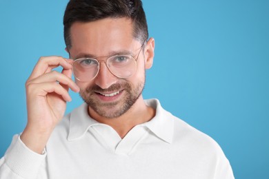 Portrait of happy man in stylish glasses on light blue background. Space for text