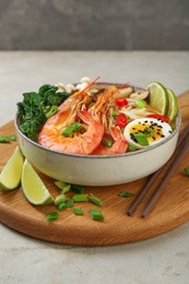 Delicious ramen with shrimps, egg in bowl and chopsticks on light textured table. Noodle soup