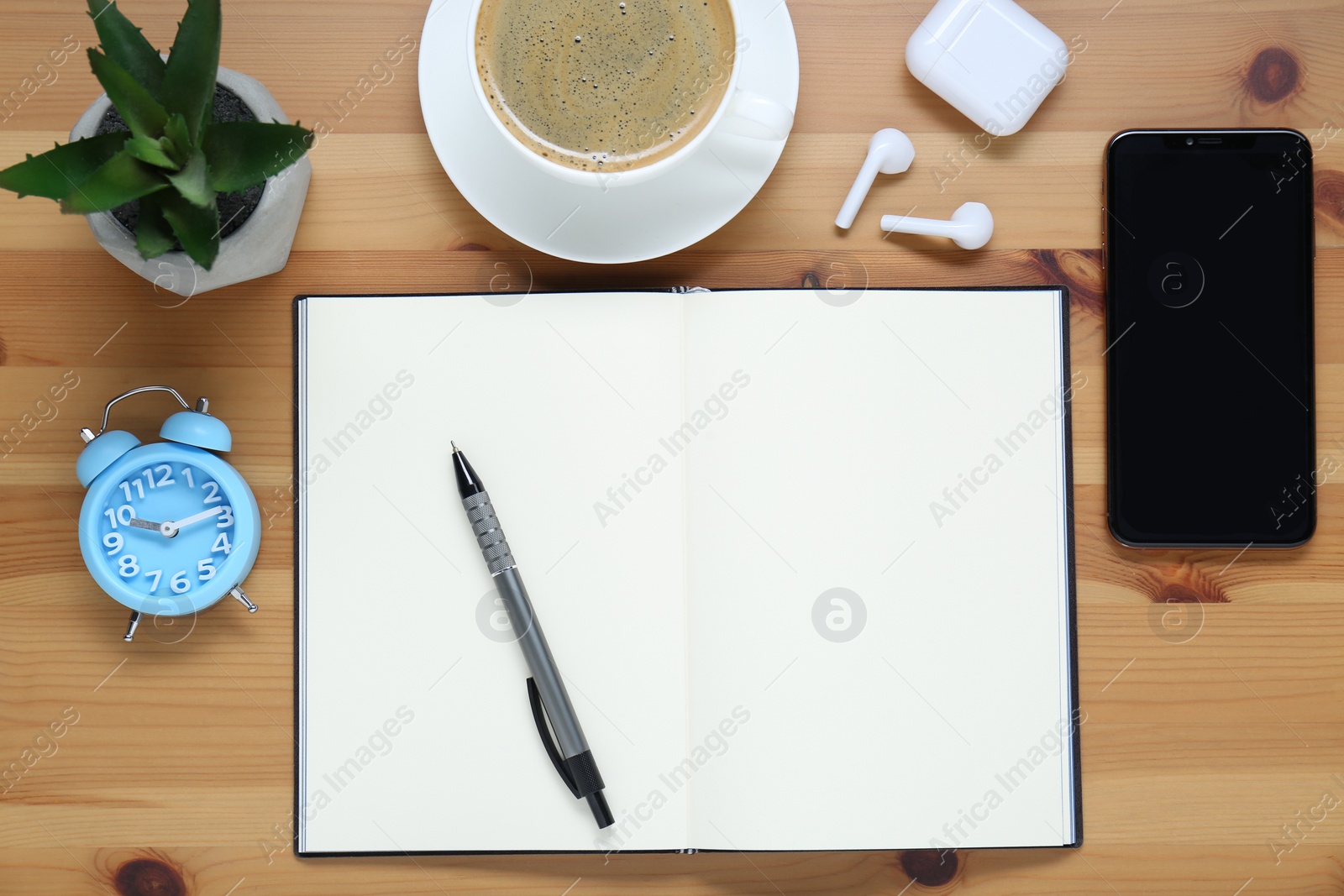 Photo of Empty notebook, coffee, houseplant, alarm clock and smartphone on wooden table, flat lay