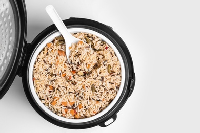 Photo of Delicious rice with vegetables and spoon in modern multi cooker on white background, top view