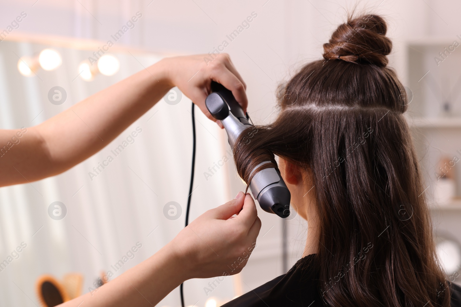 Photo of Hairdresser using curling hair iron while working with woman in salon, closeup