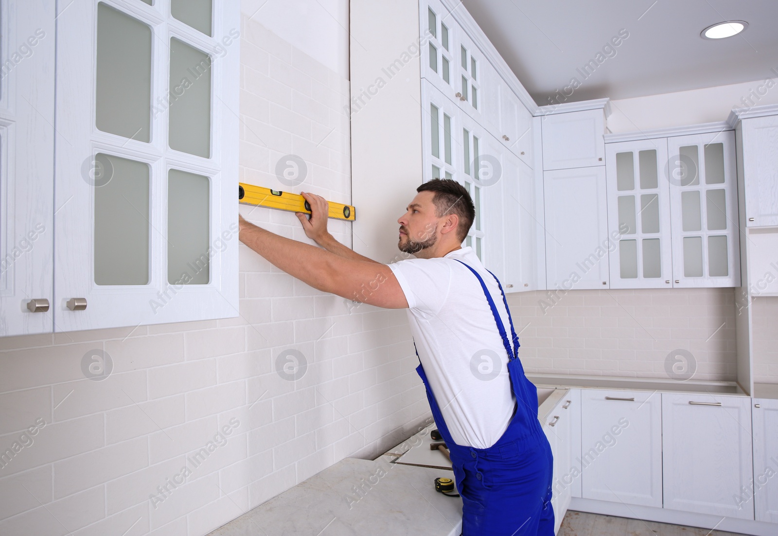 Photo of Worker using spirit level while installing new furniture in kitchen