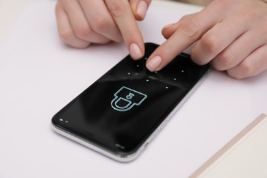 Woman unlocking smartphone with blocked screen at white table, closeup