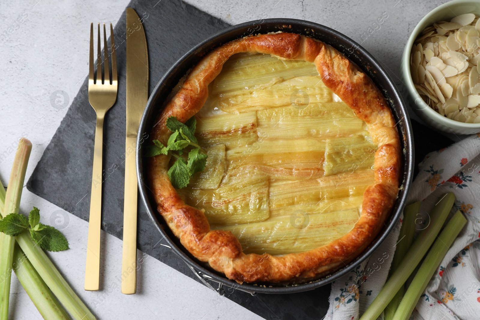 Photo of Freshly baked rhubarb pie, stalks and cutlery on light grey table, flat lay