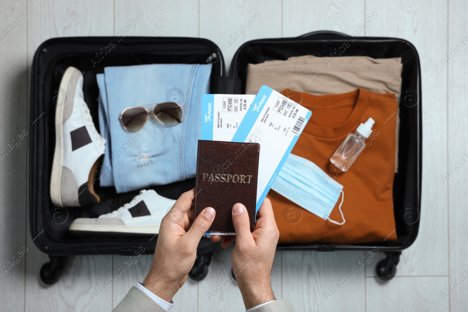 Photo of Man holding passport with tickets above open suitcase, top view. Travel during quarantine