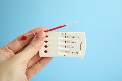 Photo of Woman holding disposable express test for hepatitis and pipette with blood on light blue background, closeup