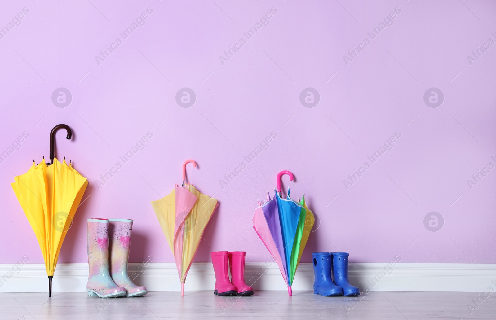 Photo of Beautiful umbrellas and gumboots on floor near color wall with space for design