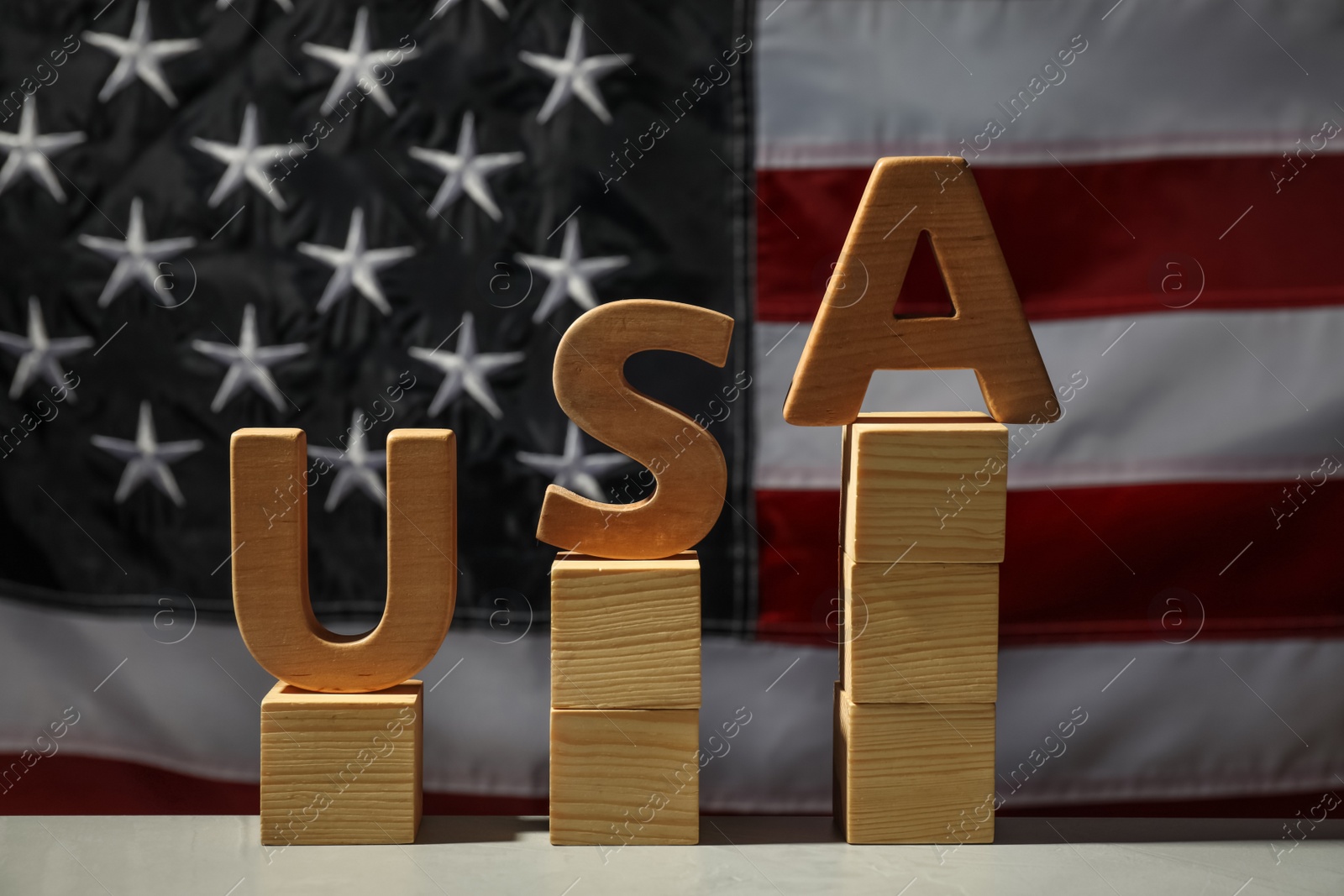 Photo of Word USA made with wooden letters and cubes on light table against national flag
