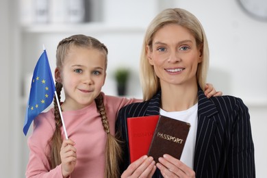 Immigration. Happy woman with her daughter holding passports and flag of European Union indoors