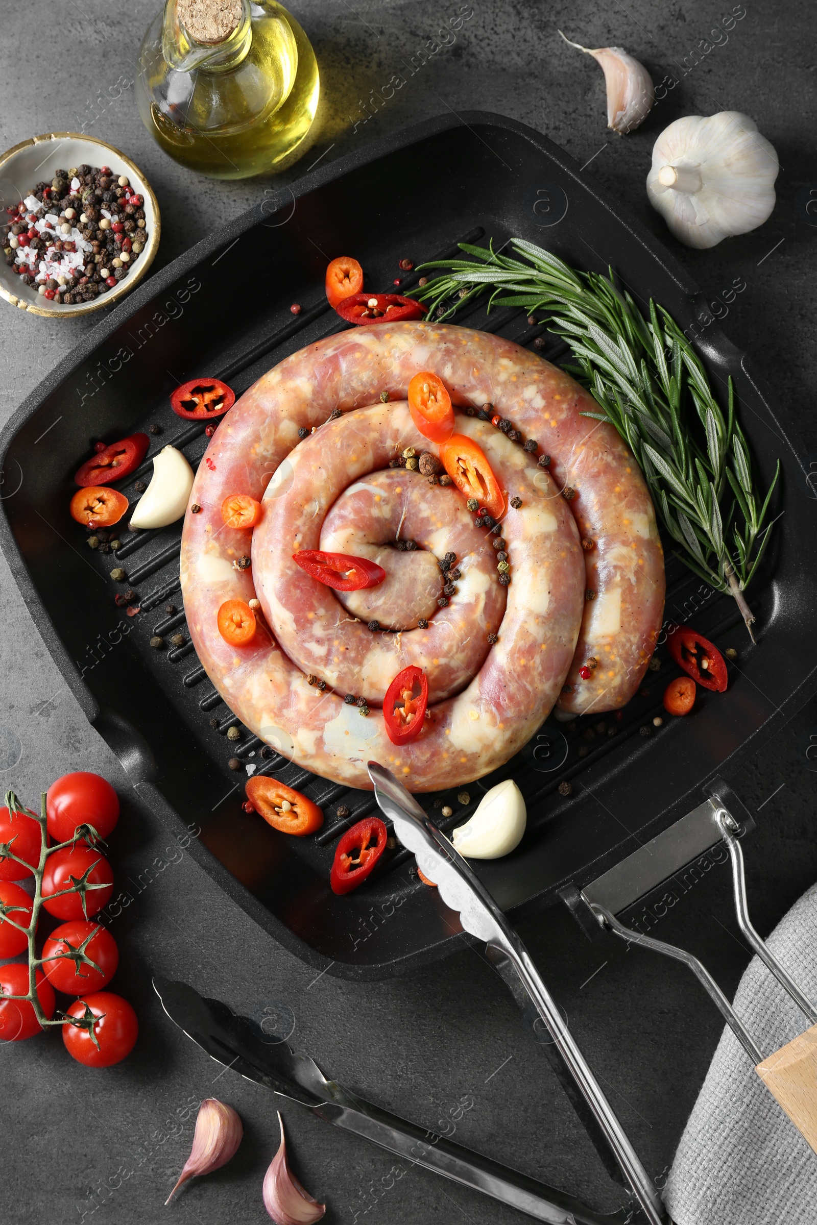 Photo of Pan with raw homemade sausage, spices, oil and tomatoes on grey table, flat lay