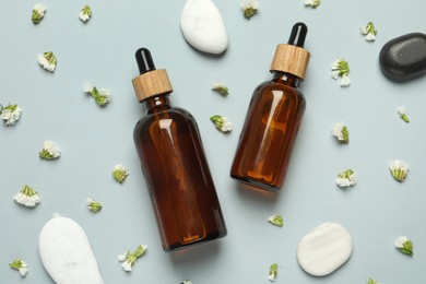 Photo of Flat lay composition with bottles of face serum, spa stones and beautiful flowers on light grey background