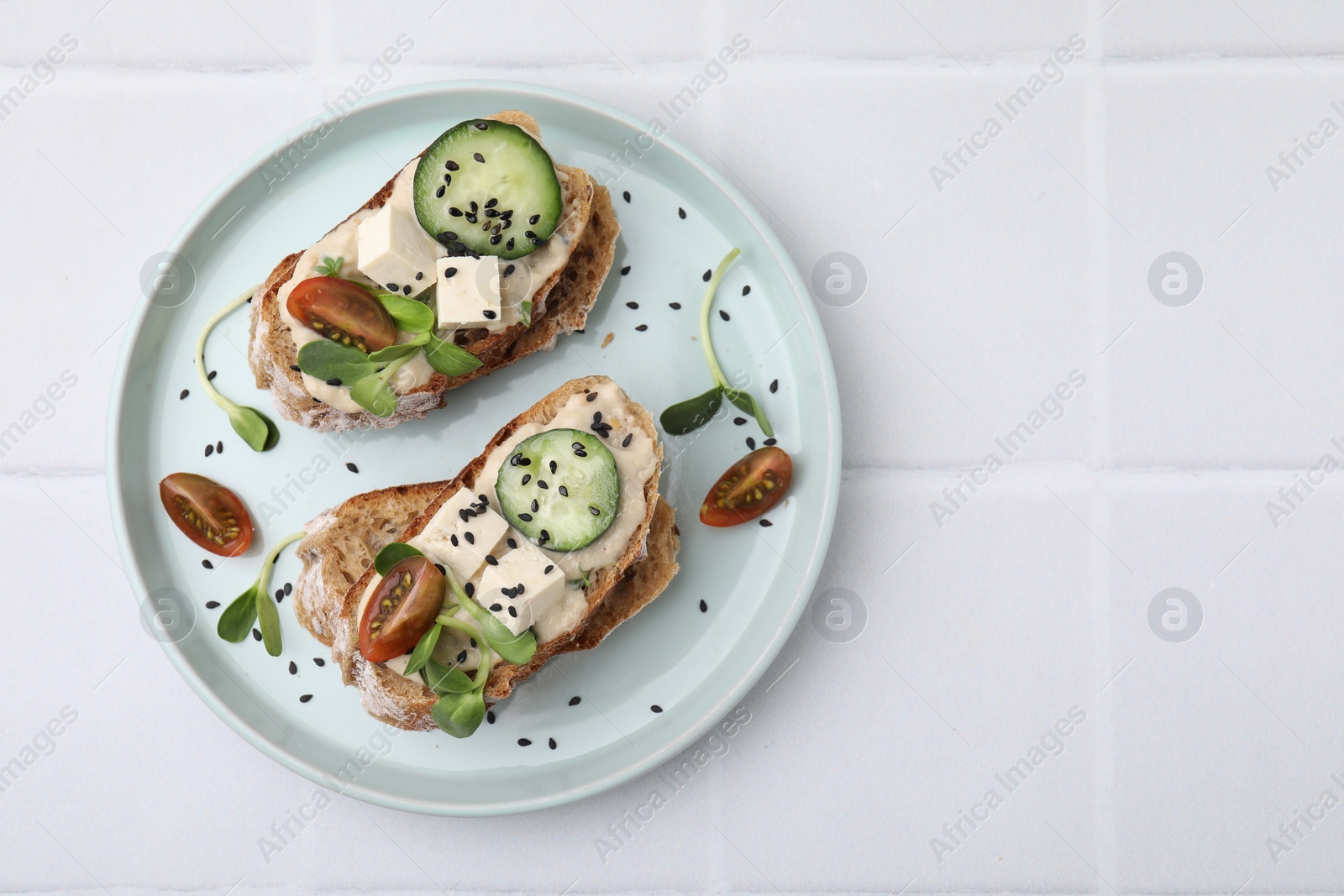 Photo of Tasty vegan sandwiches with tofu, cucumber, tomato and sesame seeds on white tiled table, top view. Space for text