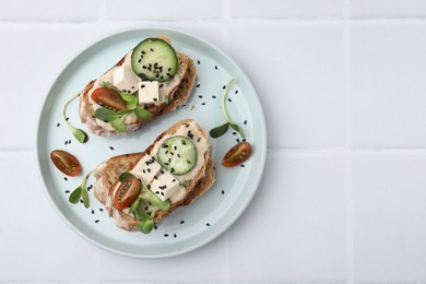 Tasty vegan sandwiches with tofu, cucumber, tomato and sesame seeds on white tiled table, top view. Space for text