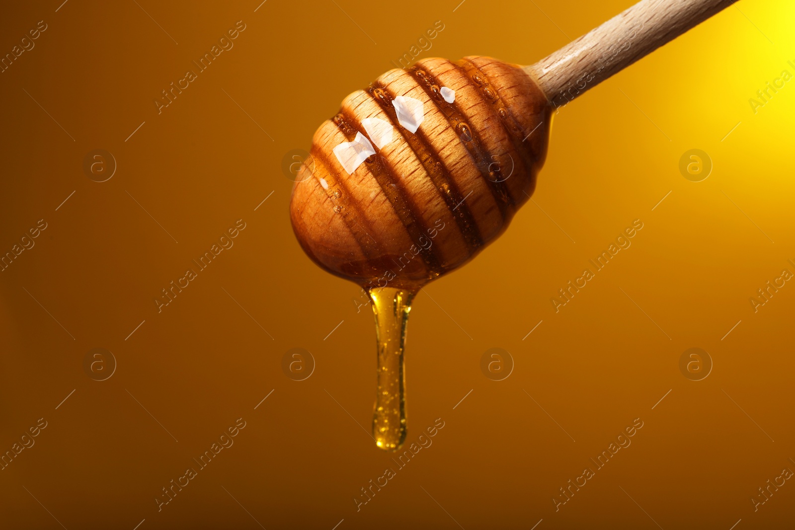 Photo of Pouring honey from dipper against golden background