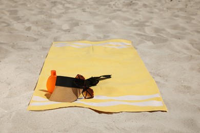 Photo of Beach towel with visor cap, sunglasses and sunscreen on sand