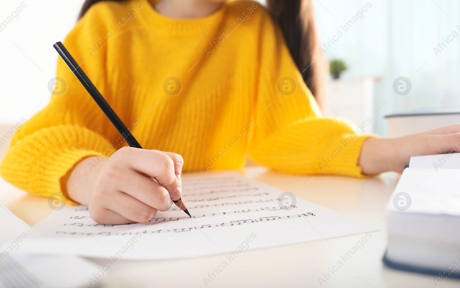 Photo of Little girl writing music notes at table, closeup
