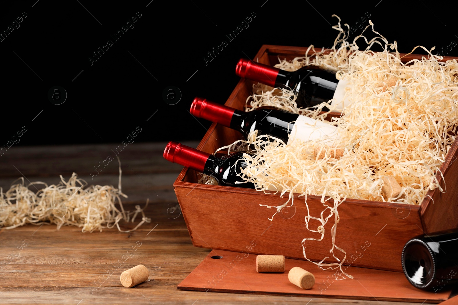 Photo of Box with wine bottles on wooden table against black background. Space for text