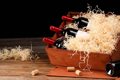 Box with wine bottles on wooden table against black background. Space for text