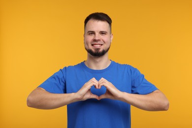 Photo of Man showing heart gesture with hands on golden background