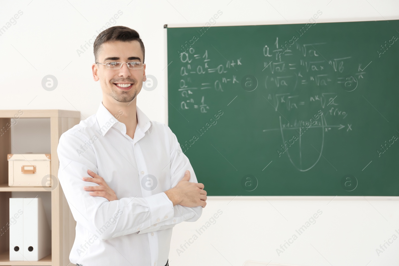 Photo of Young male teacher standing near blackboard in classroom