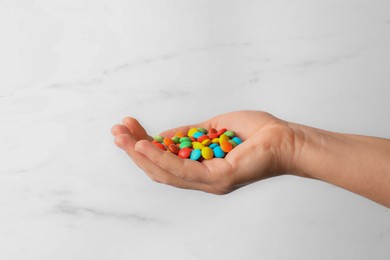 Photo of Woman with handful of tasty colorful candies on white marble background, closeup