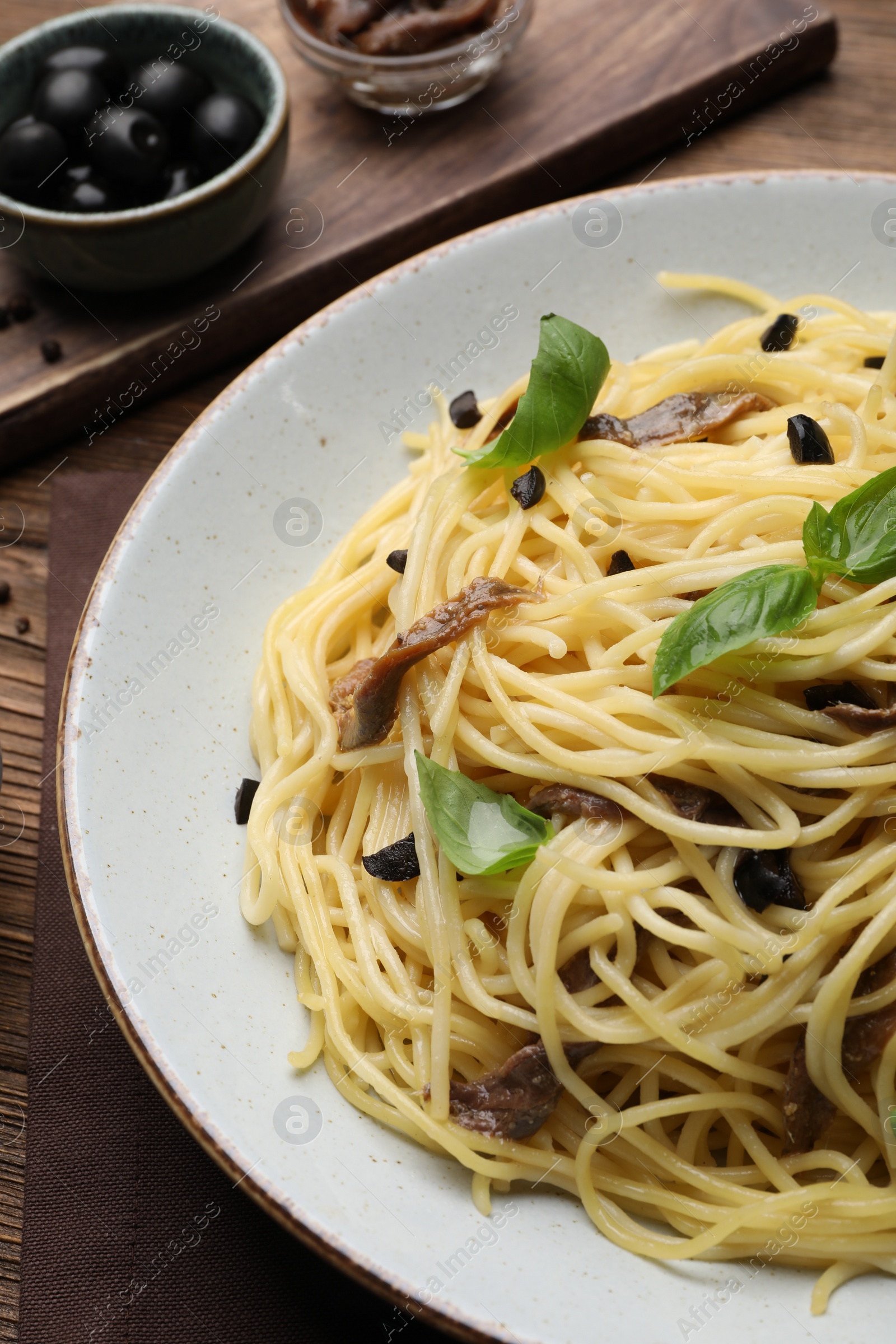 Photo of Delicious pasta with anchovies, olives and basil on wooden table, closeup