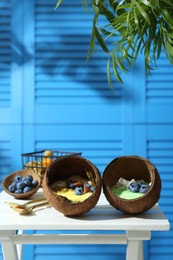 Photo of Tasty smoothie bowl served in coconut shells on white wooden table
