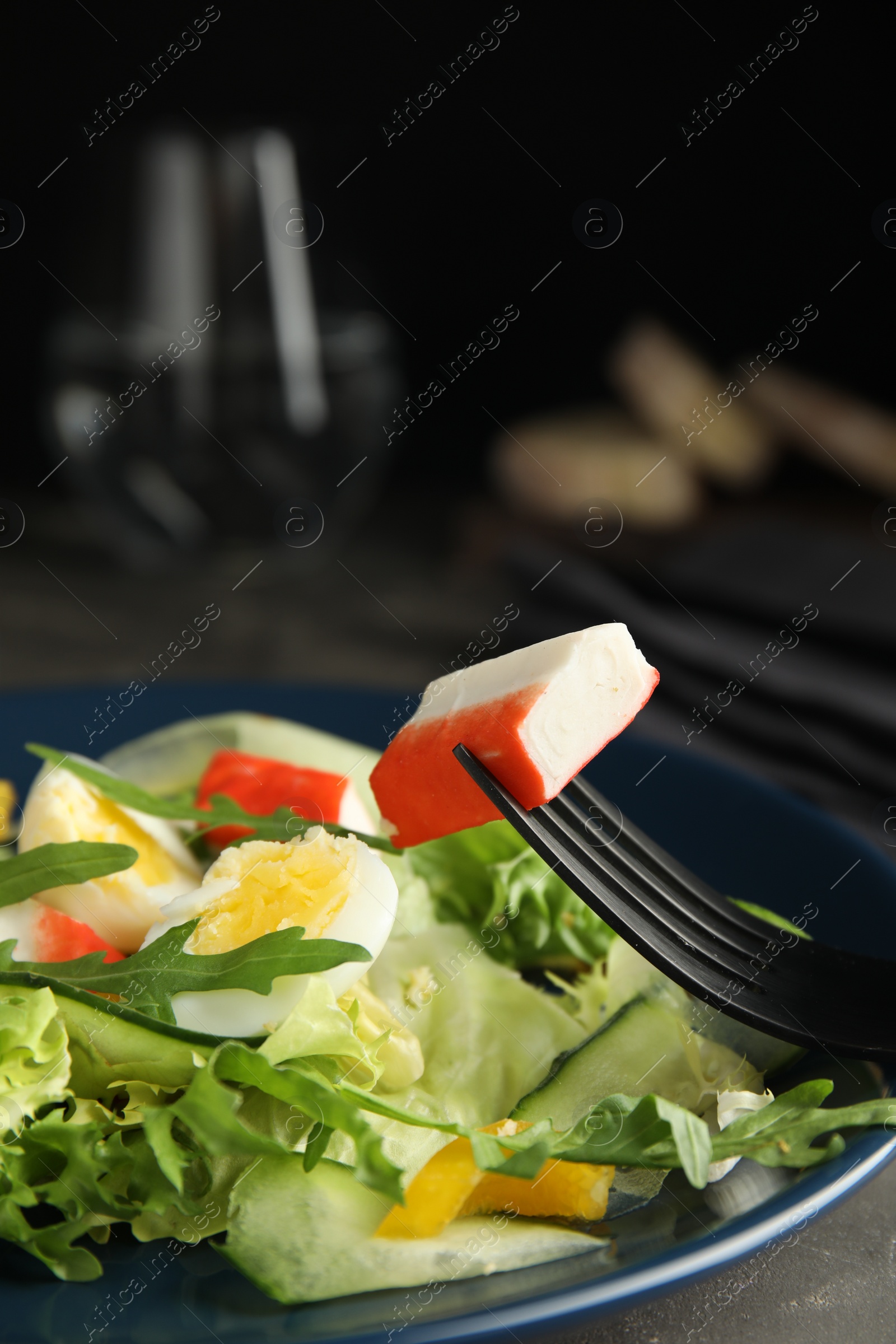 Photo of Delicious salad with crab sticks and lettuce on dark blue plate, closeup