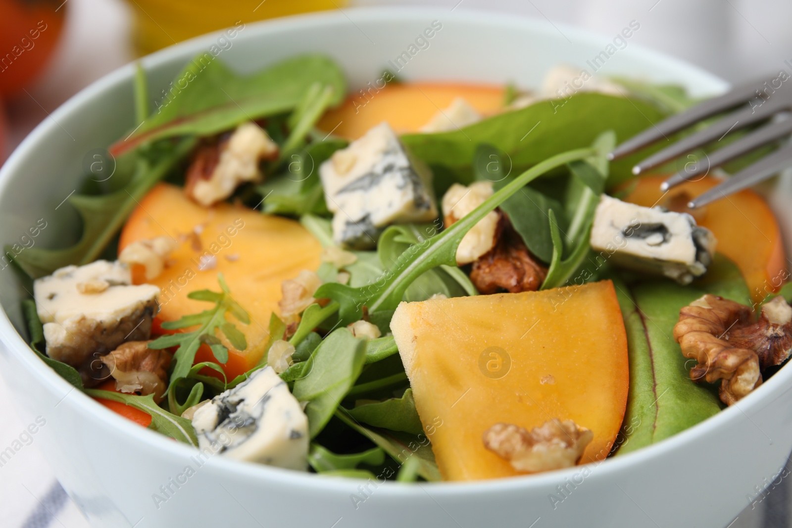 Photo of Tasty salad with persimmon, blue cheese and walnuts served on table, closeup