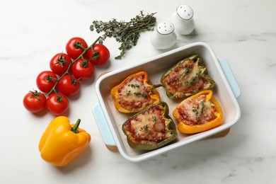 Photo of Tasty stuffed peppers in dish and ingredients on white marble table, flat lay