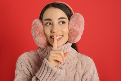 Beautiful young woman wearing earmuffs on red background