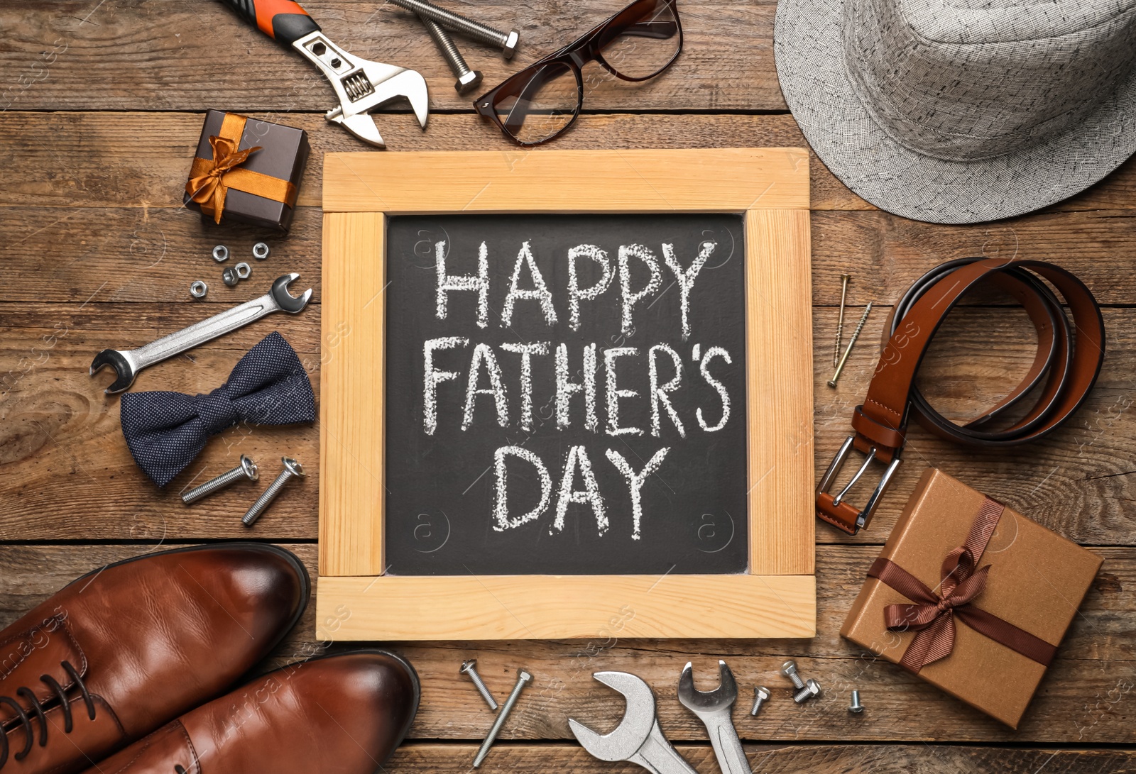 Photo of Small chalkboard with phrase HAPPY FATHER'S DAY, 
different tools and male accessories on wooden background, flat lay