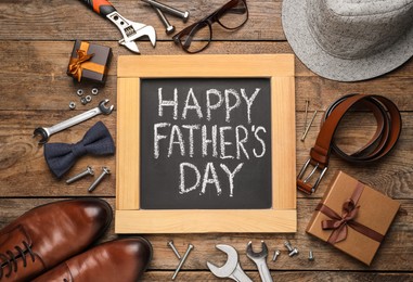 Photo of Small chalkboard with phrase HAPPY FATHER'S DAY, 
different tools and male accessories on wooden background, flat lay